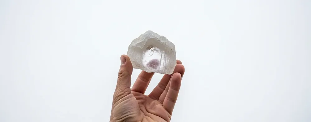 En hånd holder en ru, mælket krystal op mod en helt grå himmel